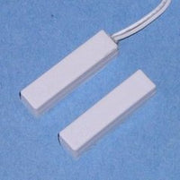 Two white 1 1/4 inch surface mount magnetic alarm contact switches with one featuring an attached white cable